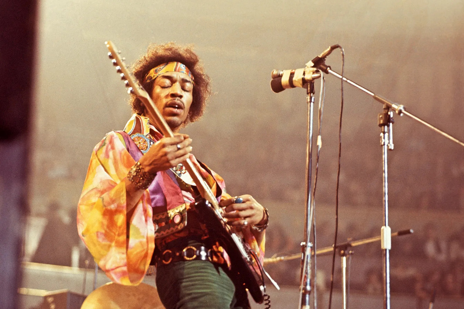 An action shot of Jimi Hendrix performing on a stadium stage with his guitar in hand. guiat 