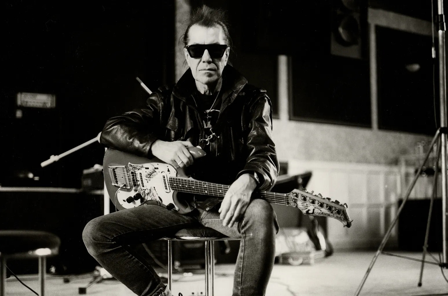 Black and white picture of artist, Link Wray, posing with his guitar and wearing black sunglasses