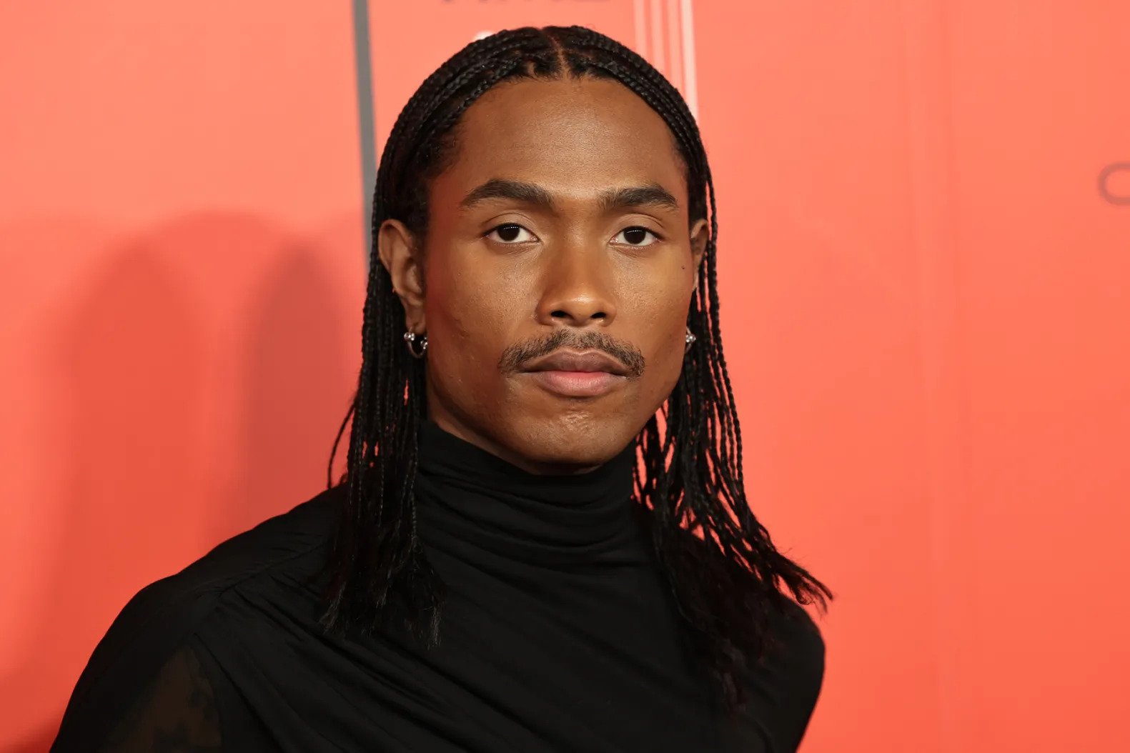 Steve Lacy posting for a portrait with orange background in an all black outfit
