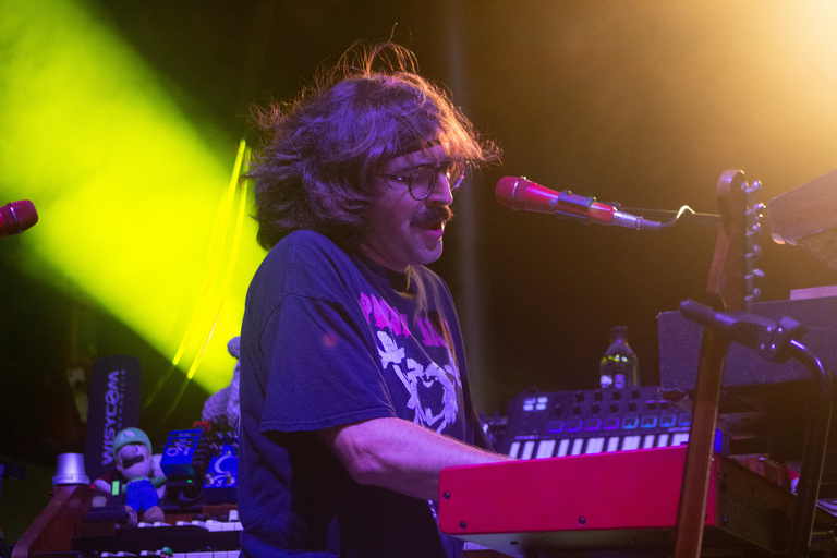 Keys player for Goose on stage with yellow lighting.