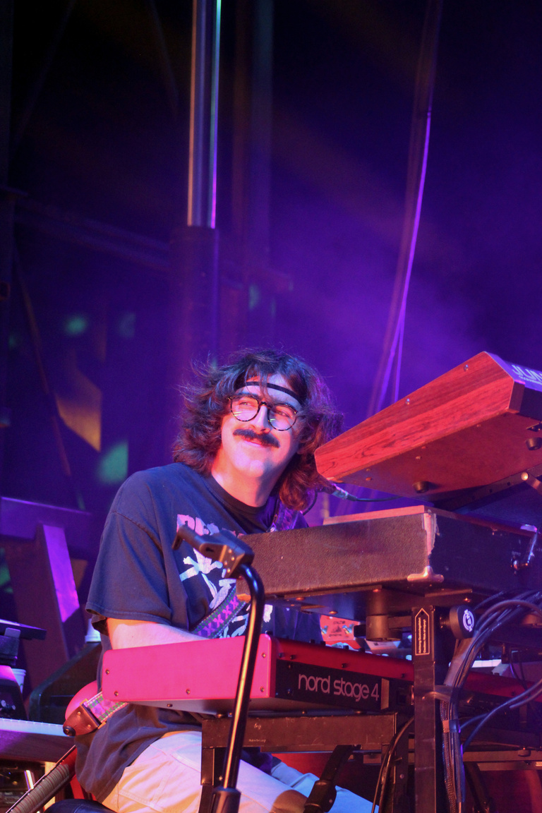 Keys player on stage, smiling at the crowd. Red keyboard with purple lighting