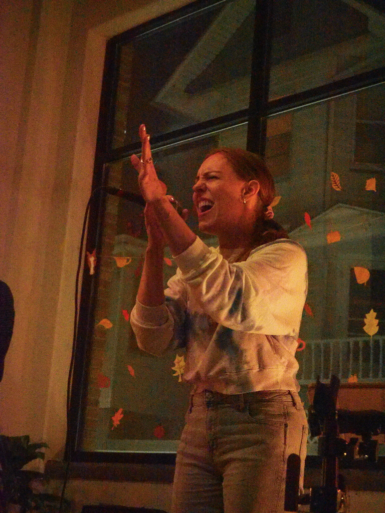 Up close image of riverglen performing. Blue long sleeve, jeans, holding microphone with other hand in the air