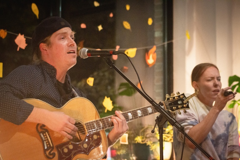 Up close image of River Glen performing with guitar and fall decoration in the background.