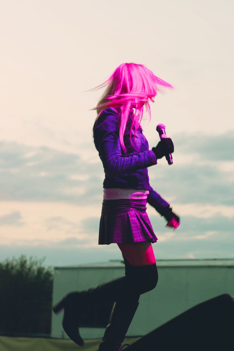 Cowgirl Clue on stage in pink lighting with sky behind her.