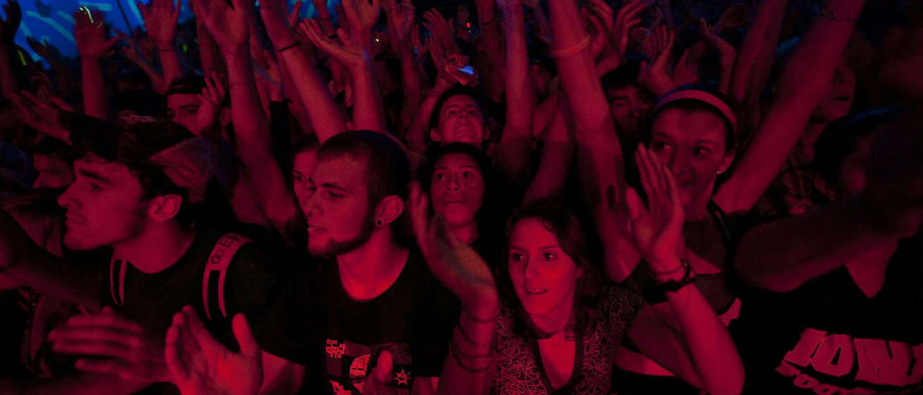 Students in the front row of a concert bathed in red stage lights, dancing